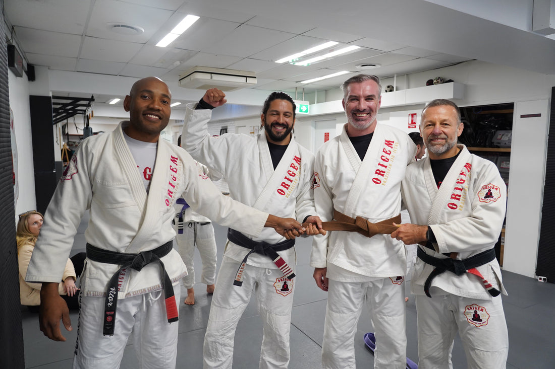Brazilian Jiu-Jitsu practitioners posing together in front of the Origem martial arts academy logo