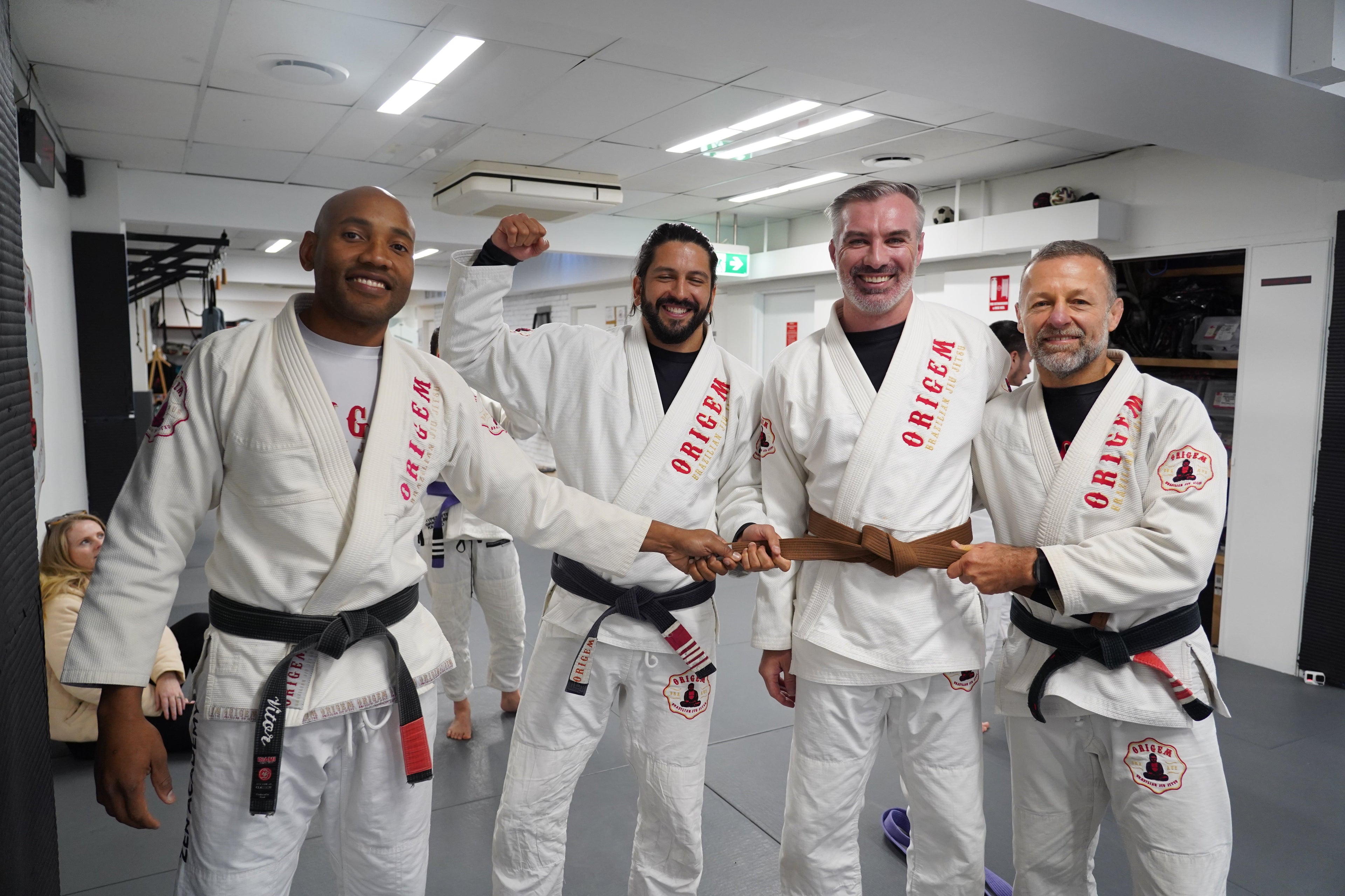 Brazilian Jiu-Jitsu practitioners posing together in front of the Origem martial arts academy logo